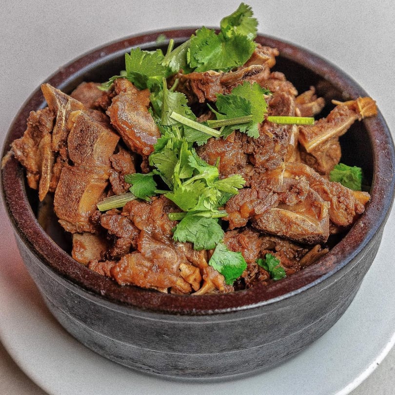 Braised lamb stew with fresh cilantro in a dark ceramic bowl on a white plate.