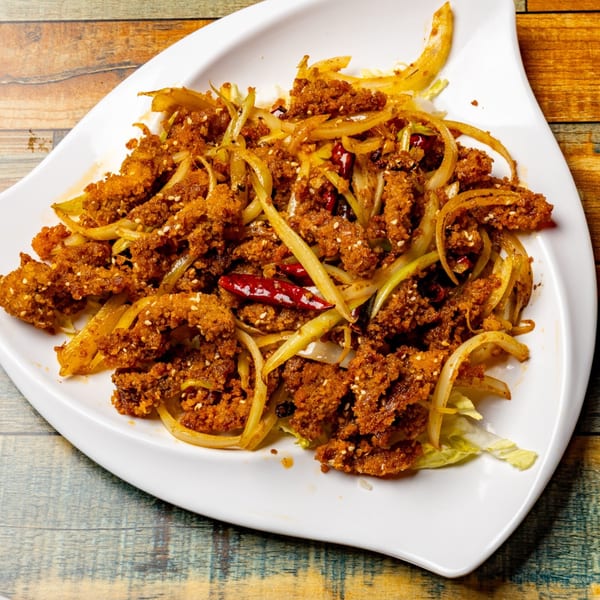 Crispy fried chicken pieces with sliced onions, red chilies, and sesame seeds on a white plate.