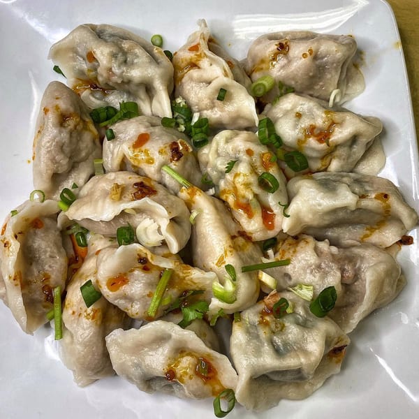 A plate of steamed dumplings drizzled with chili oil and garnished with chopped green onions.