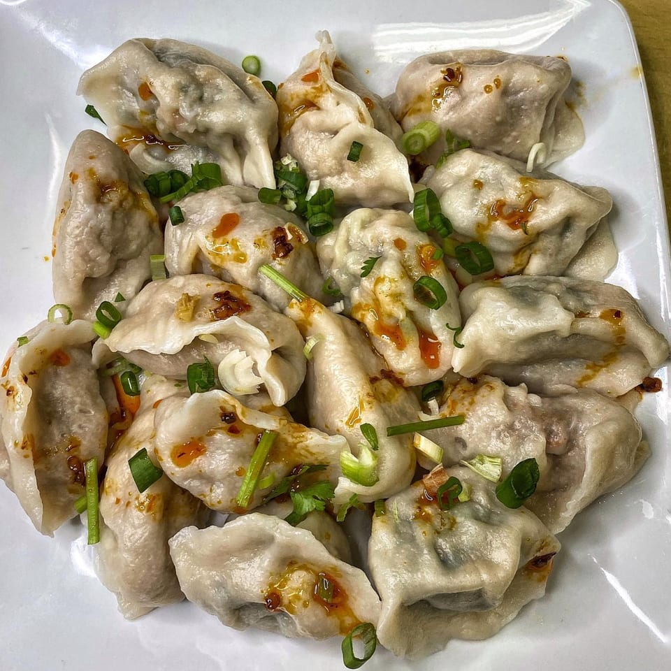 A plate of steamed dumplings drizzled with chili oil and garnished with chopped green onions.