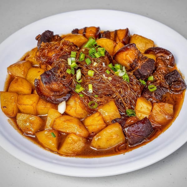 Braised pork belly with potatoes and glass noodles, garnished with chopped scallions on a white plate.