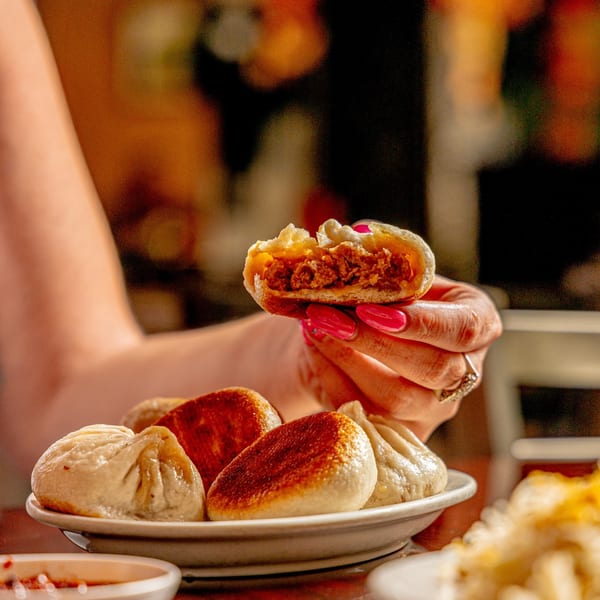 A hand holding a half-eaten dumpling, revealing a savory meat filling, with more dumplings on a plate.