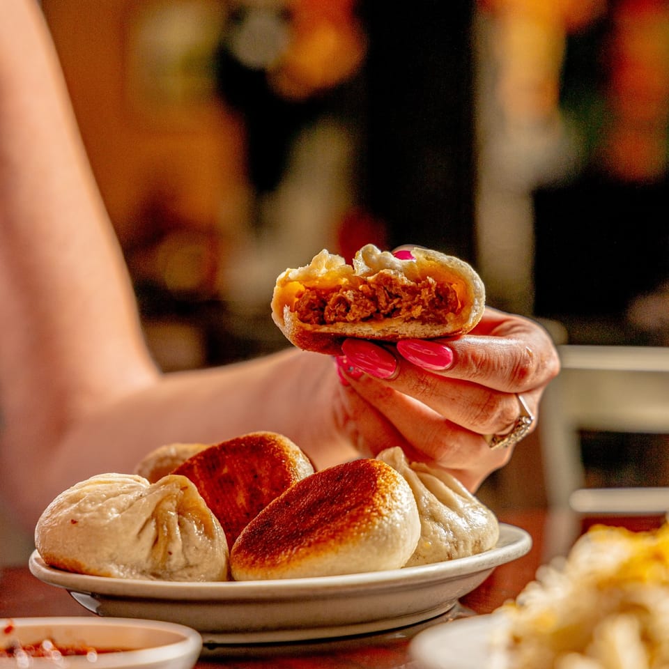 A hand holding a half-eaten dumpling, revealing a savory meat filling, with more dumplings on a plate.
