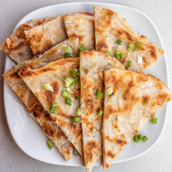 Golden-brown scallion pancakes, cut into triangles and garnished with fresh green onions on a white plate.