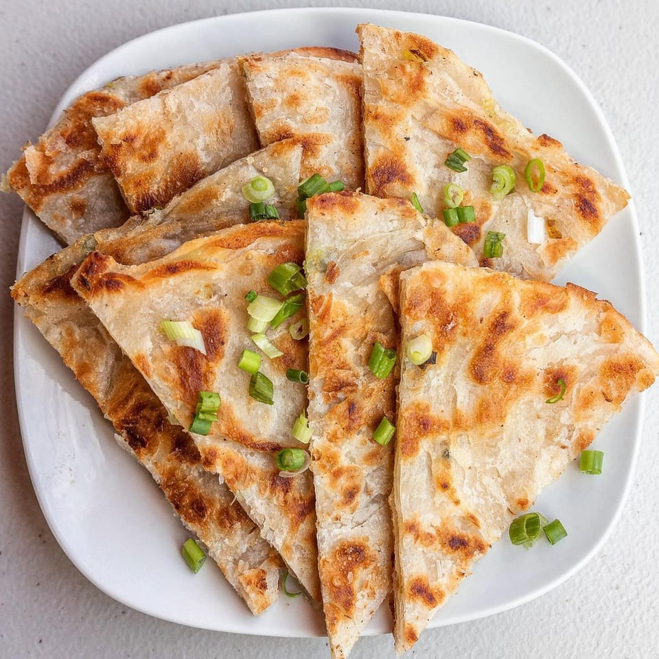 Golden-brown scallion pancakes, cut into triangles and garnished with fresh green onions on a white plate.