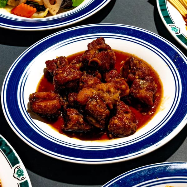 A plate of sweet and sour pork ribs in a rich, glossy sauce, on a white and blue plate.